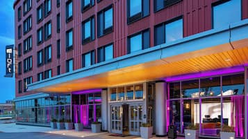 Een modern hotel met een rode gevel, grote ramen en een overdekt entreegebied met paars licht.