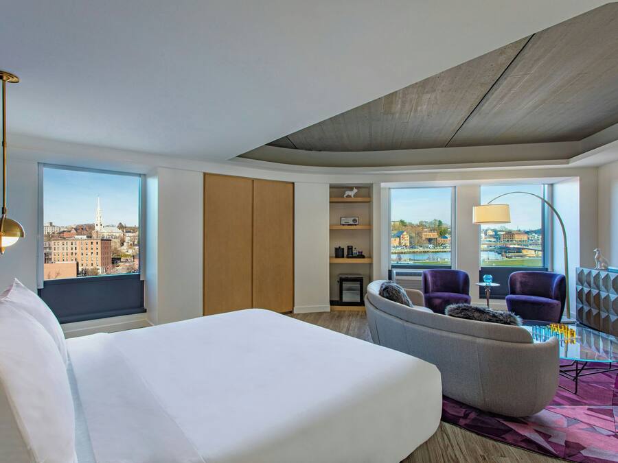 A hotel room with a bed, seating area, city view, and a television.