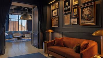 Un salon moderne avec un canapé, une table basse et une lampe. Des tableaux encadrés ornent le mur, et de grandes fenêtres offrent une vue sur l’extérieur.