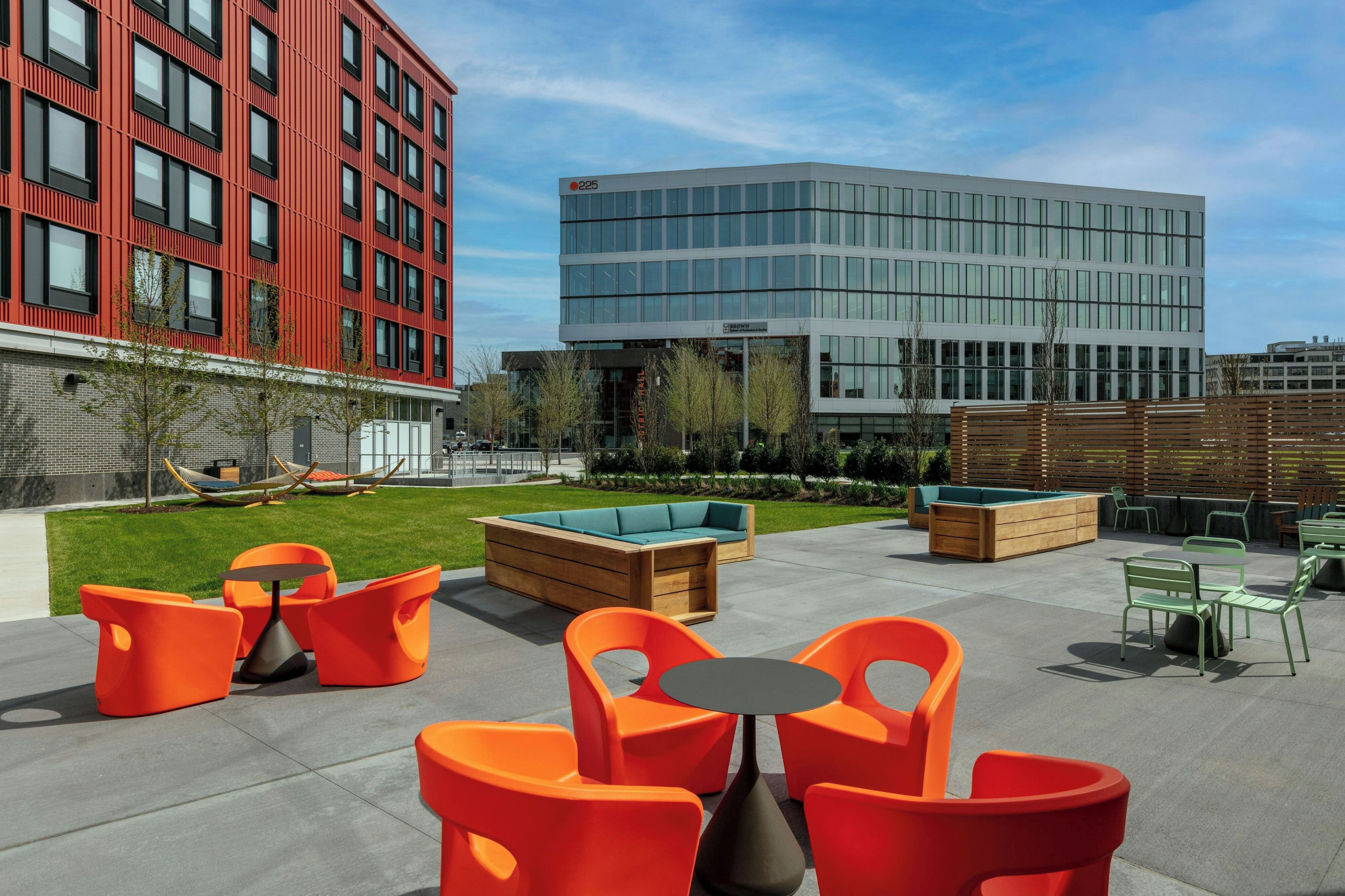 An outdoor seating area with orange chairs and tables, a wooden bench, and a pool table.