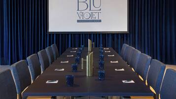 A conference room with a long table, chairs, and a screen displaying 'BLU VOET ROOFTOP BAR'.