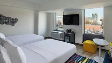 A hotel room with two beds, a desk, a chair, a TV, and a window with a city view.
