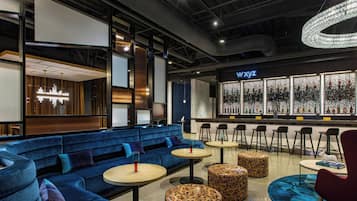 Een moderne loungeruimte met blauwe zitplaatsen, ronde tafels en een bar met verlichte flessen.