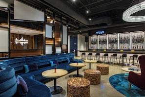 Un espace lounge moderne avec des sièges bleus, des tables rondes et un bar dont les bouteilles sont illuminées.