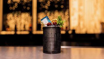 A black textured container with a blue bottle, a cherry, and mint leaves on a reflective surface.