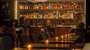 Eine Bar mit mehreren Regalen voller Spirituosenflaschen, Barhocker und Tischen mit Kerzen.