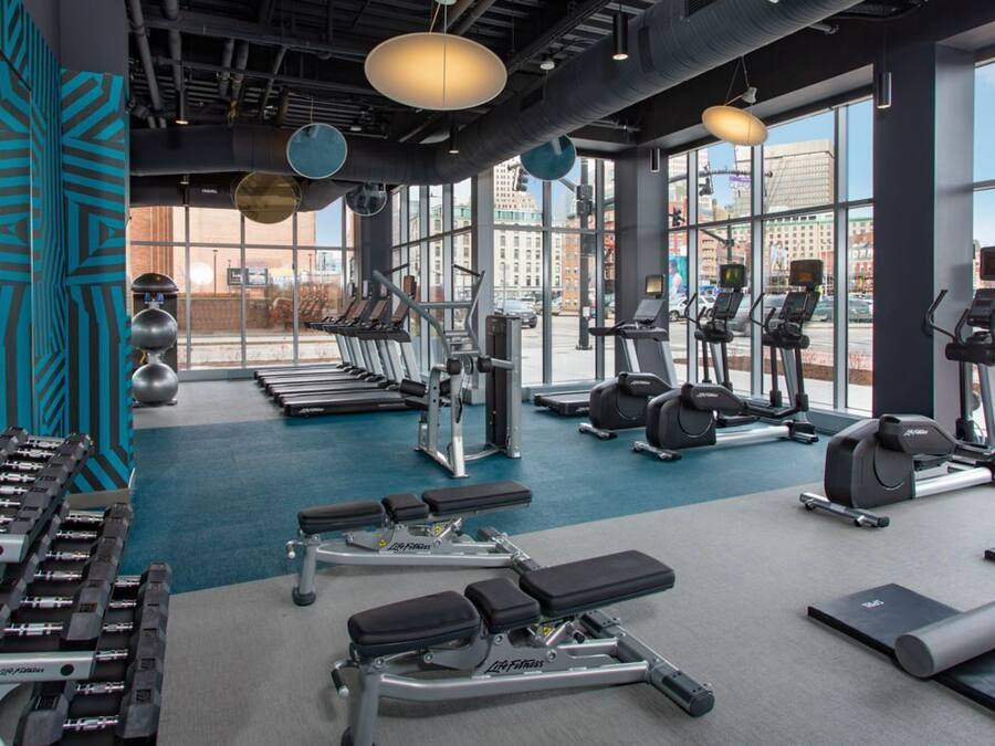 Ein modernes Fitnessstudio mit unterschiedlichen Trainingsgeräten, großen Fenstern und Blick auf die Stadt.