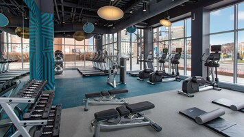 Un gimnasio moderno con diversos equipos de ejercicio, ventanas amplias y vistas a la ciudad.