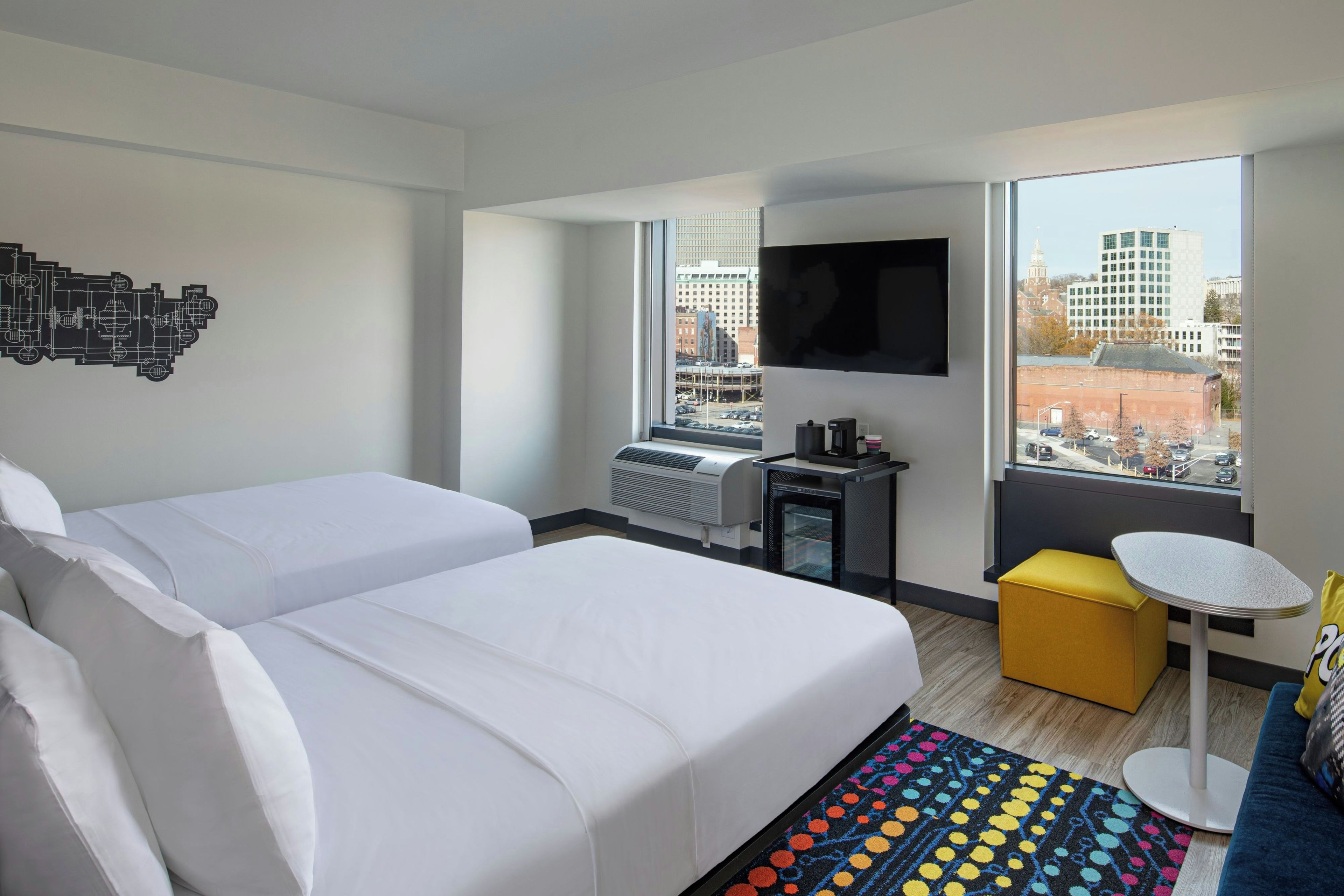 Une chambre d’hôtel avec deux lits, un bureau, une chaise, une télévision et une fenêtre donnant sur la ville.