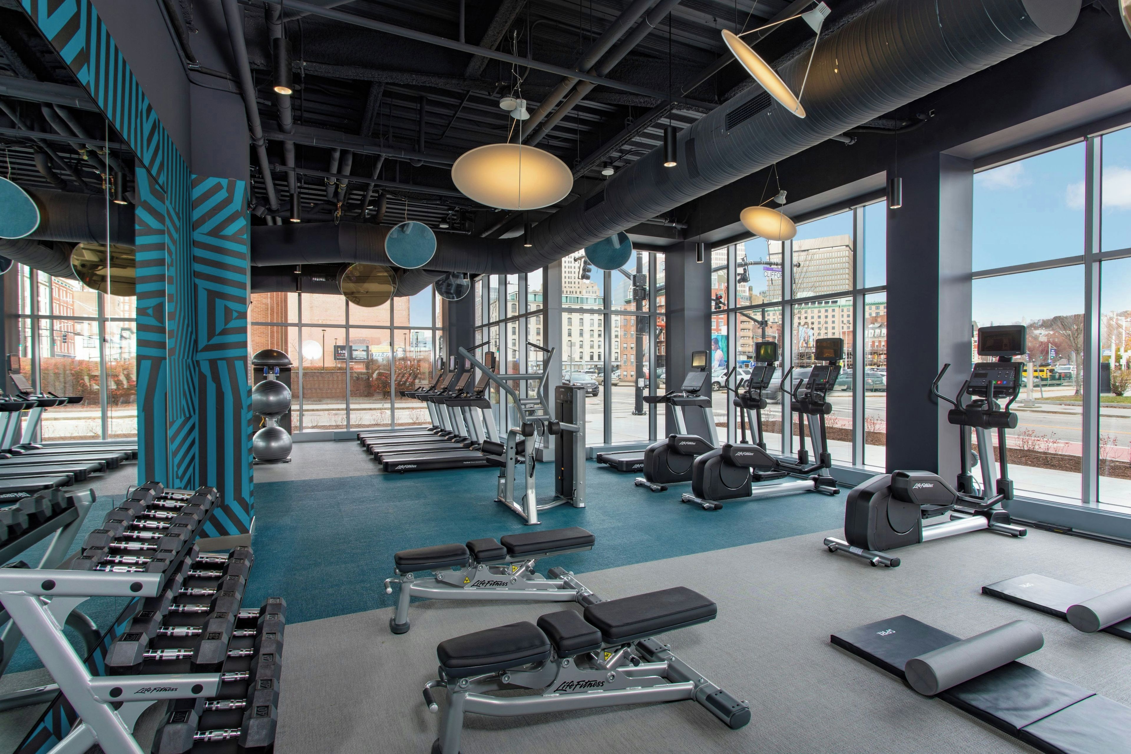 Een sportschool met diverse trainingsapparatuur, grote ramen en uitzicht op de stad.