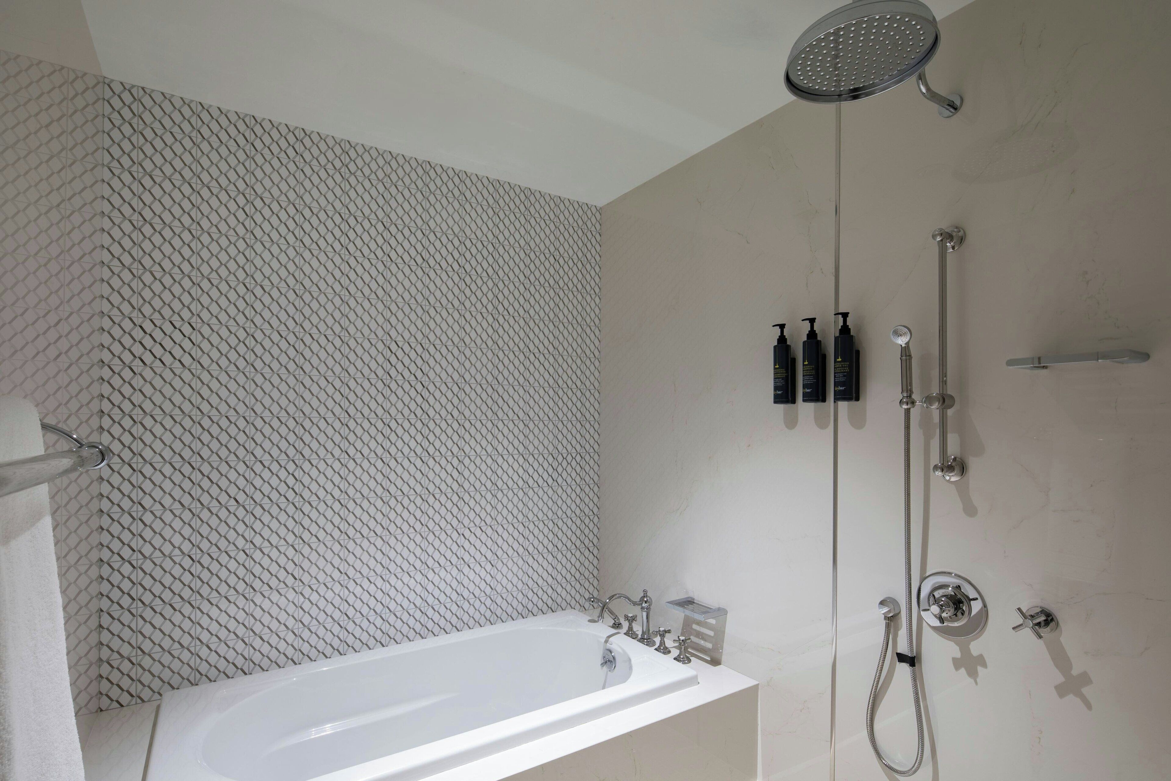 A modern bathroom with a freestanding bathtub, a showerhead, and a wall-mounted soap dispenser.