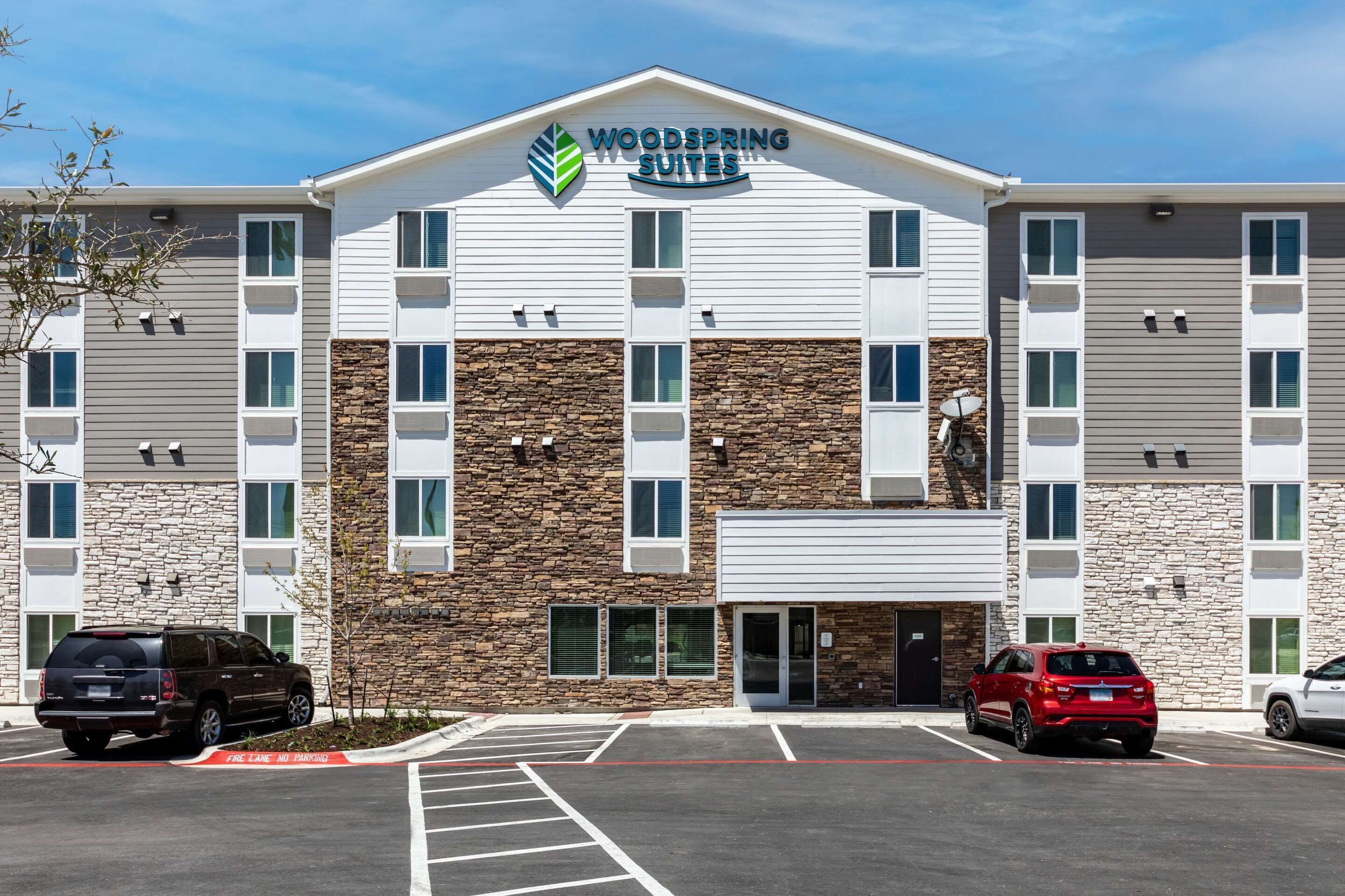 Un hotel de varios pisos con fachada de piedra y un letrero que dice 'Woodspring Suites'.