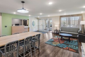 Una habitación de hotel moderna con una mesa de comedor de madera, sillas, un sofá, una mesita redonda y una alfombra colorida.