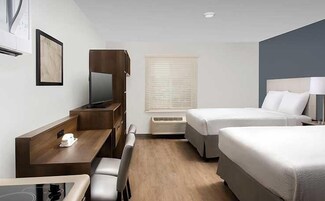 Habitación de hotel con escritorio, dos camas, televisor y ventana con persianas.