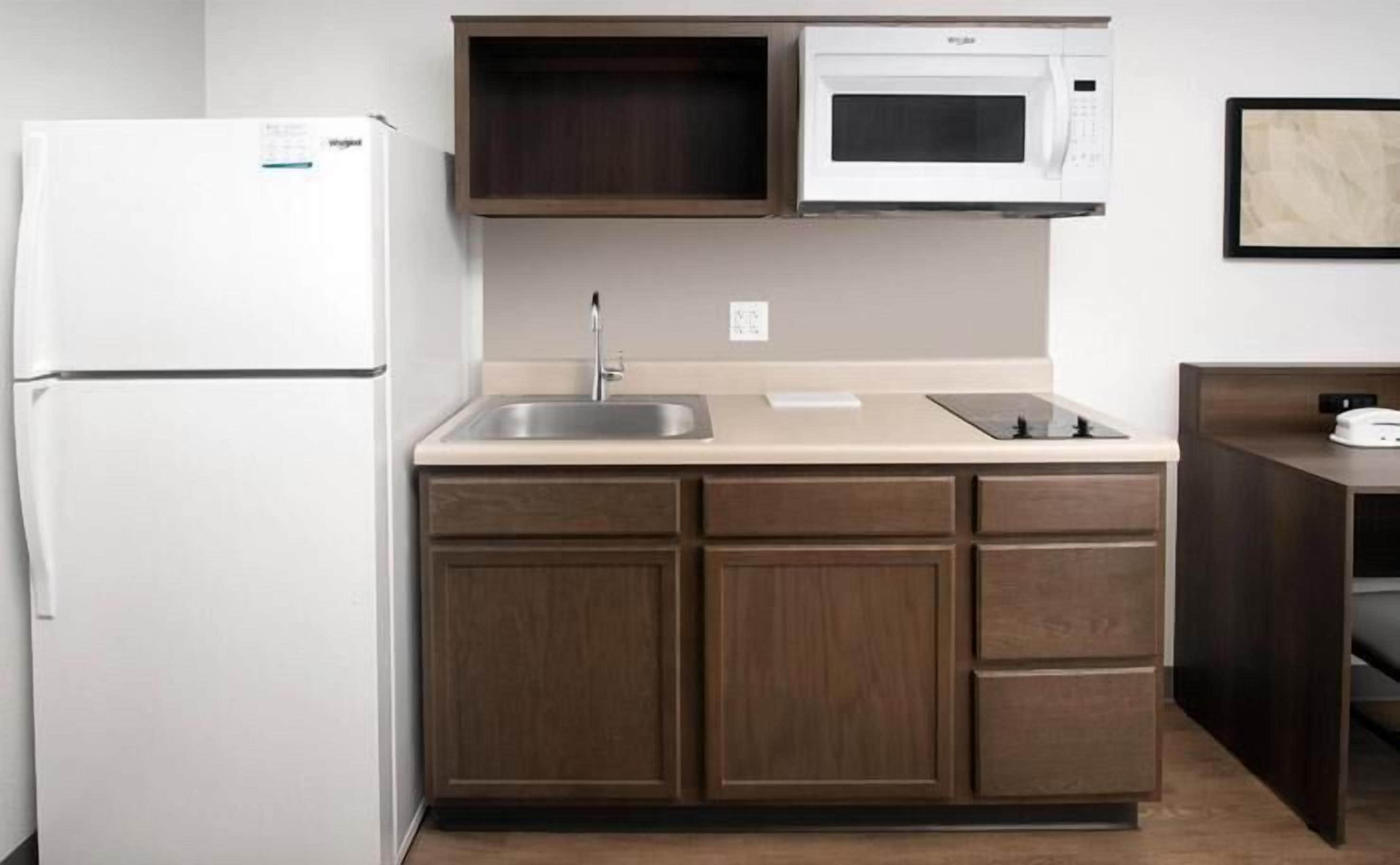 A compact kitchen with a white refrigerator, a microwave, a sink, and wooden cabinets.