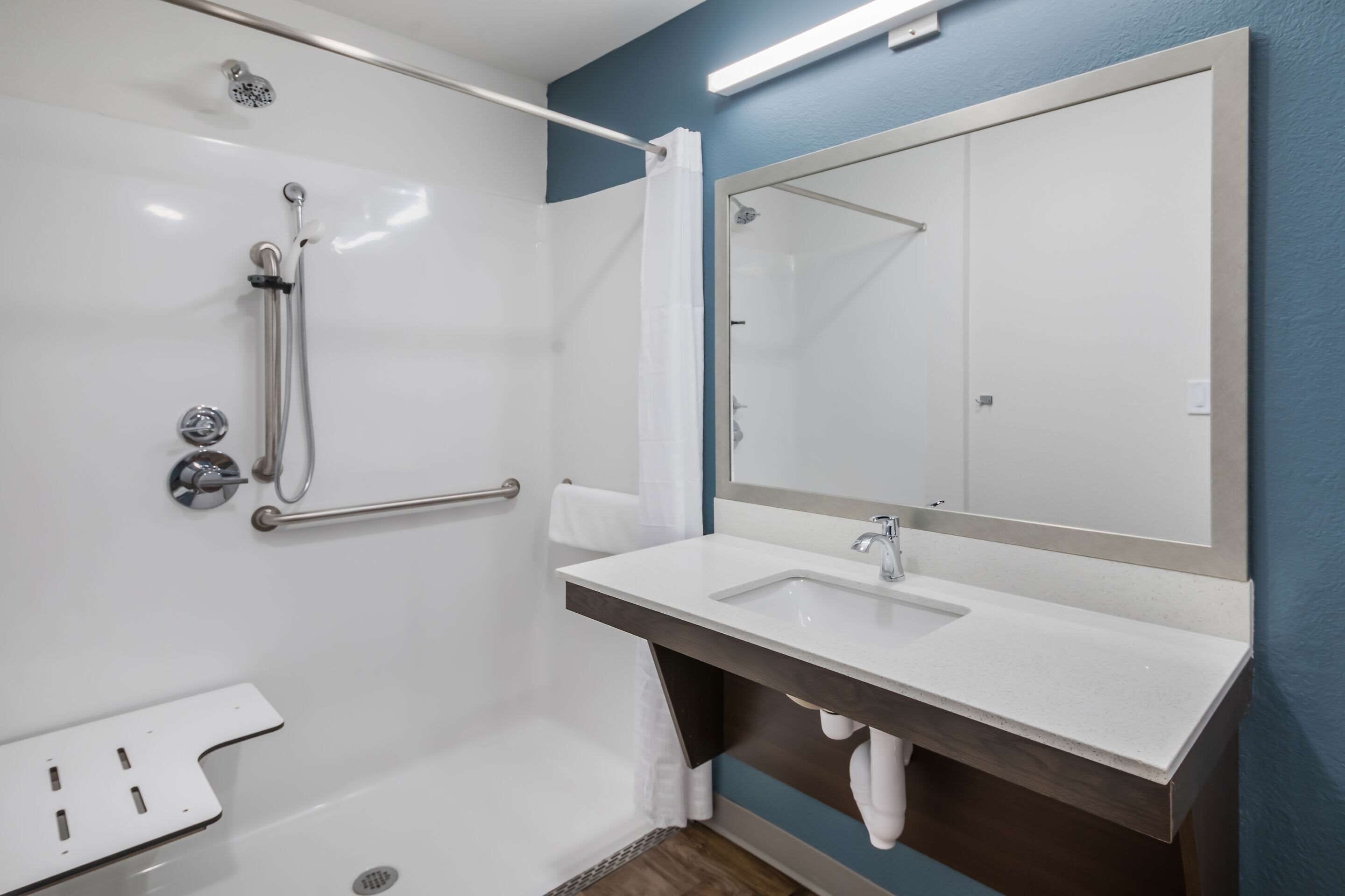 A modern bathroom with a walk-in shower, a white sink, and a large mirror.