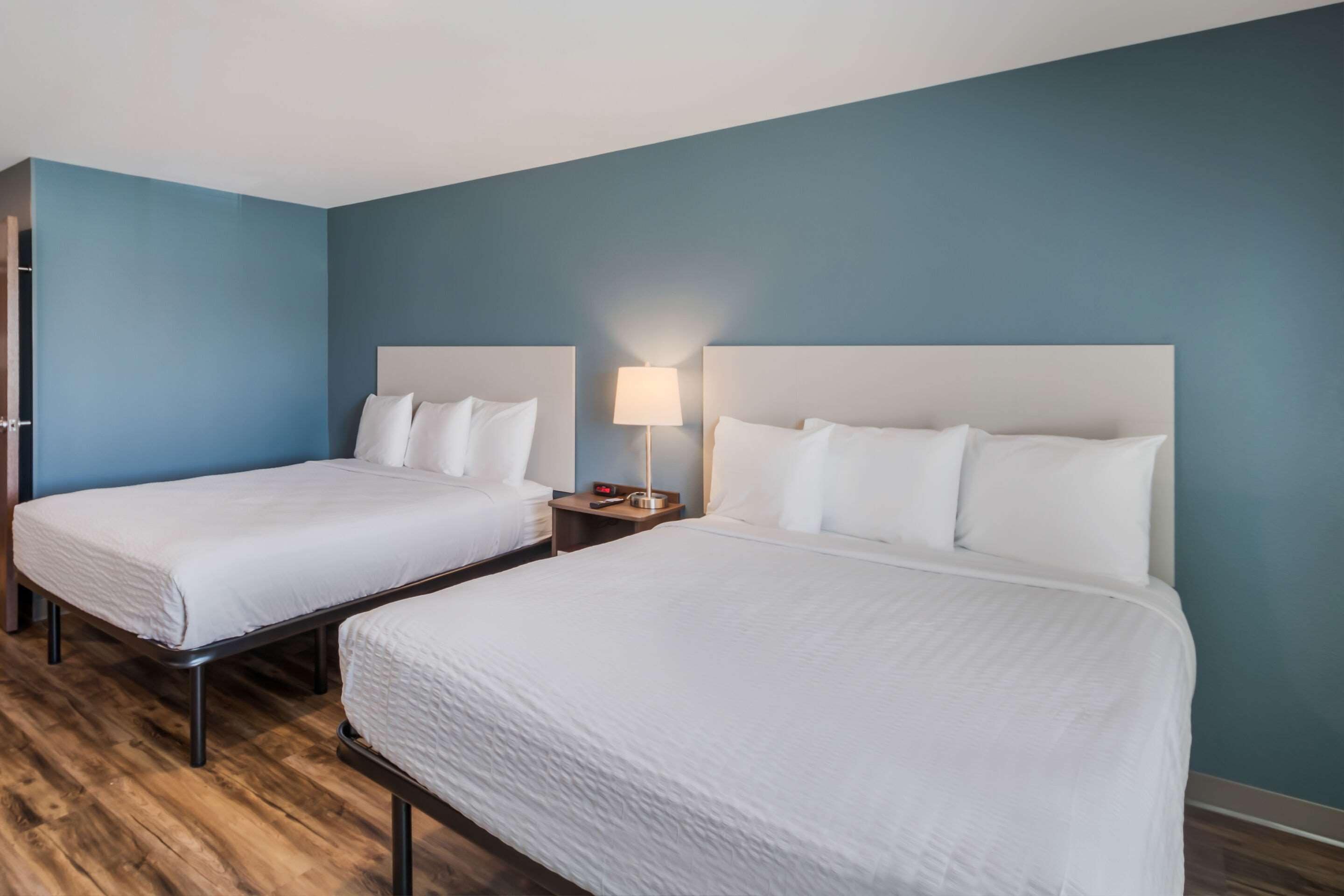 Een hotelkamer met twee bedden, een nachtkastje met een lamp en een houten vloer.