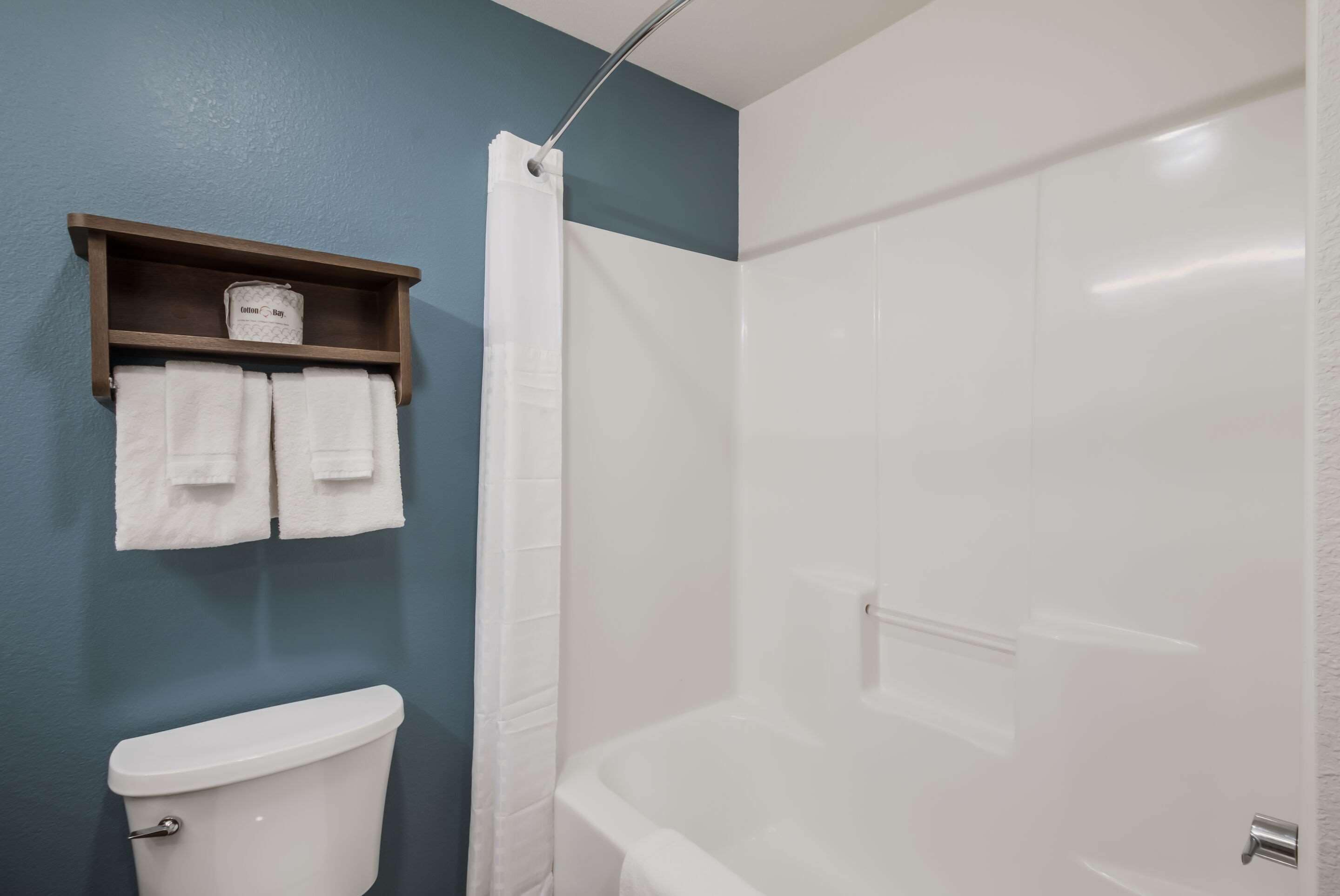A bathroom with a toilet, a shower with a curtain, and a shelf with towels.