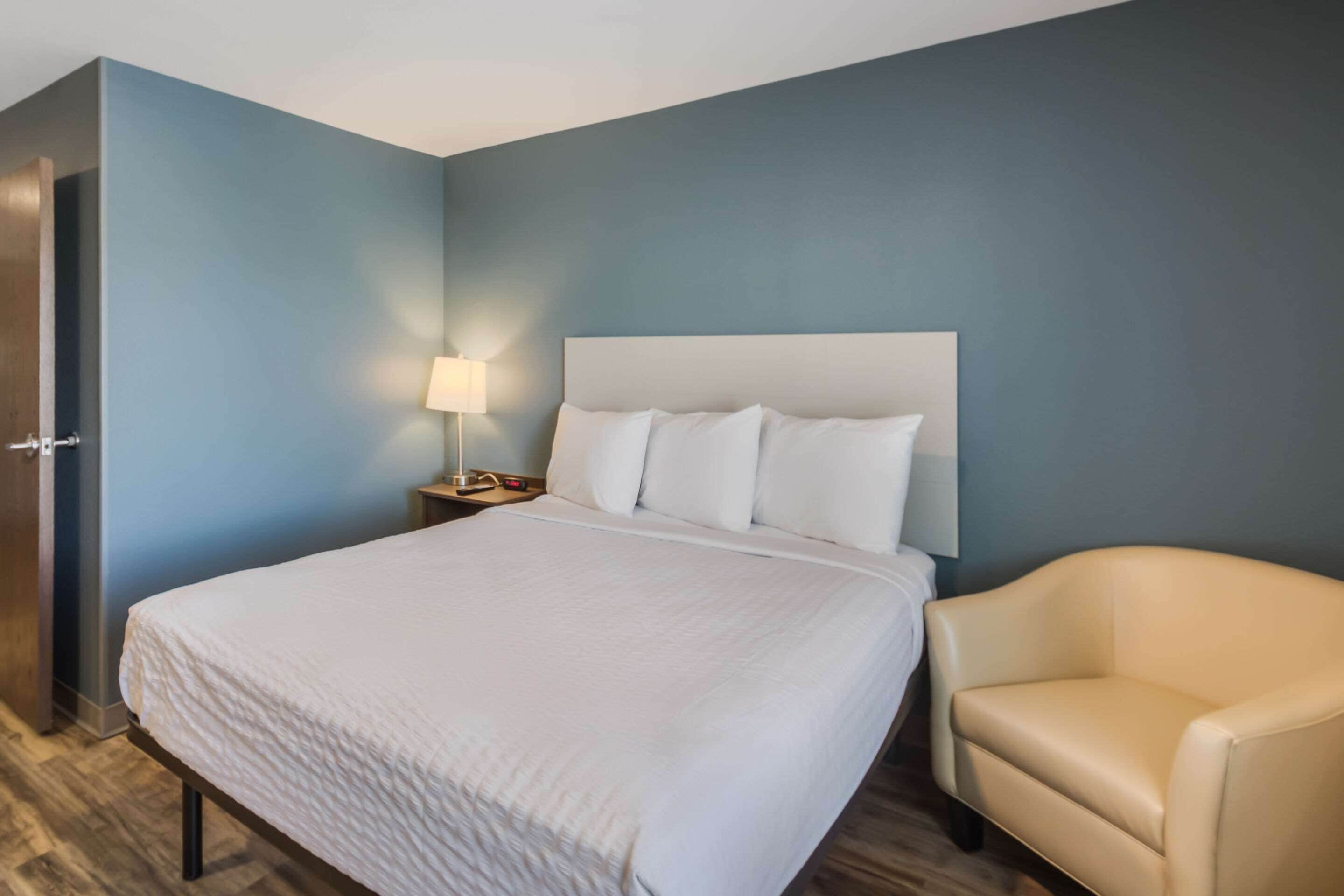 A hotel room with a large bed, a bedside table with a lamp, and a chair.