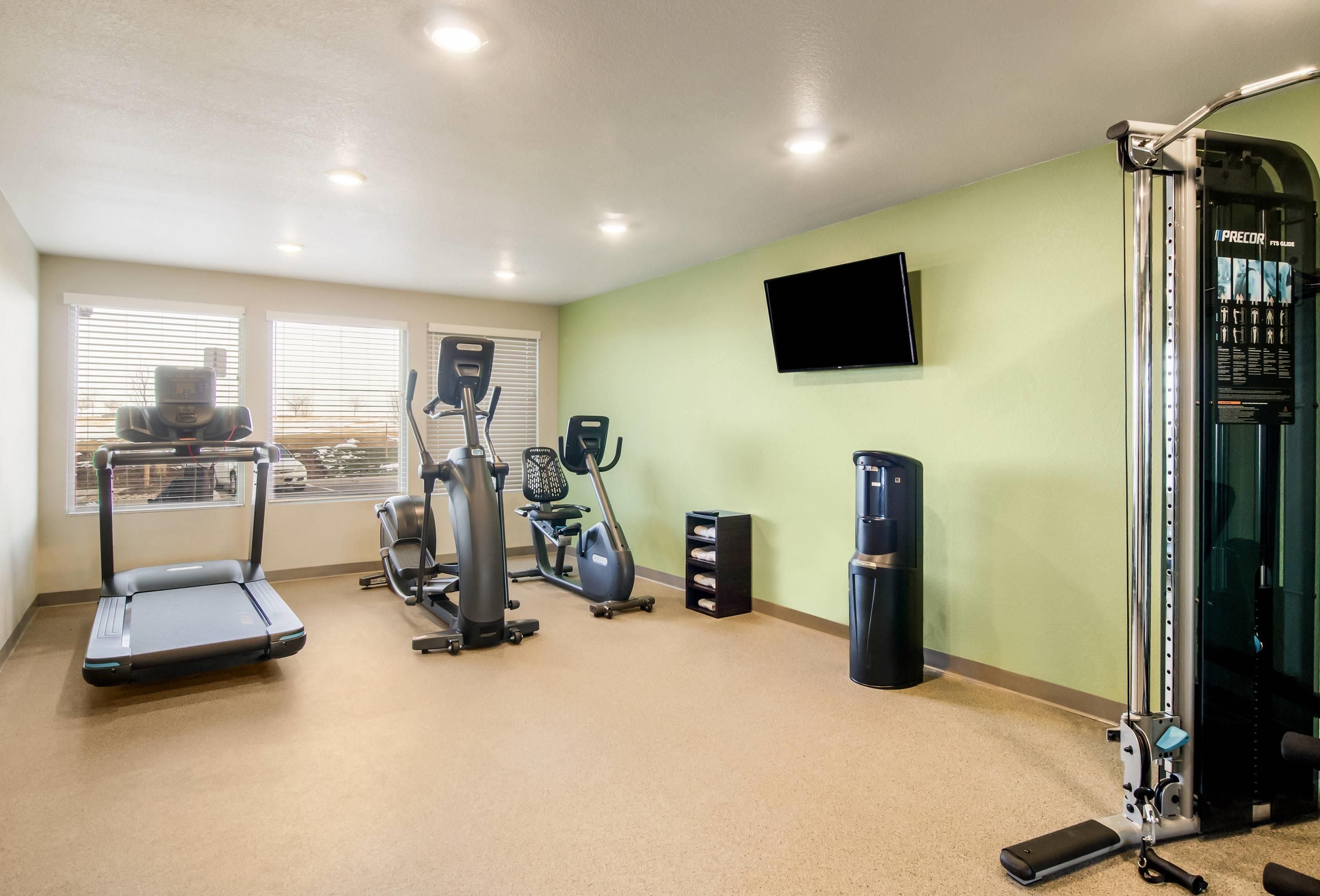 Ein Fitnessraum mit Laufband, Crosstrainer, Heimtrainer und einem an der Wand montierten Fernseher.