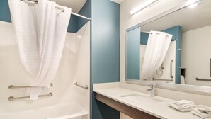 A modern bathroom with a bathtub, a sink with a mirror, and a towel rack. - WoodSpring Suites Thornton-North Denver (Thornton)