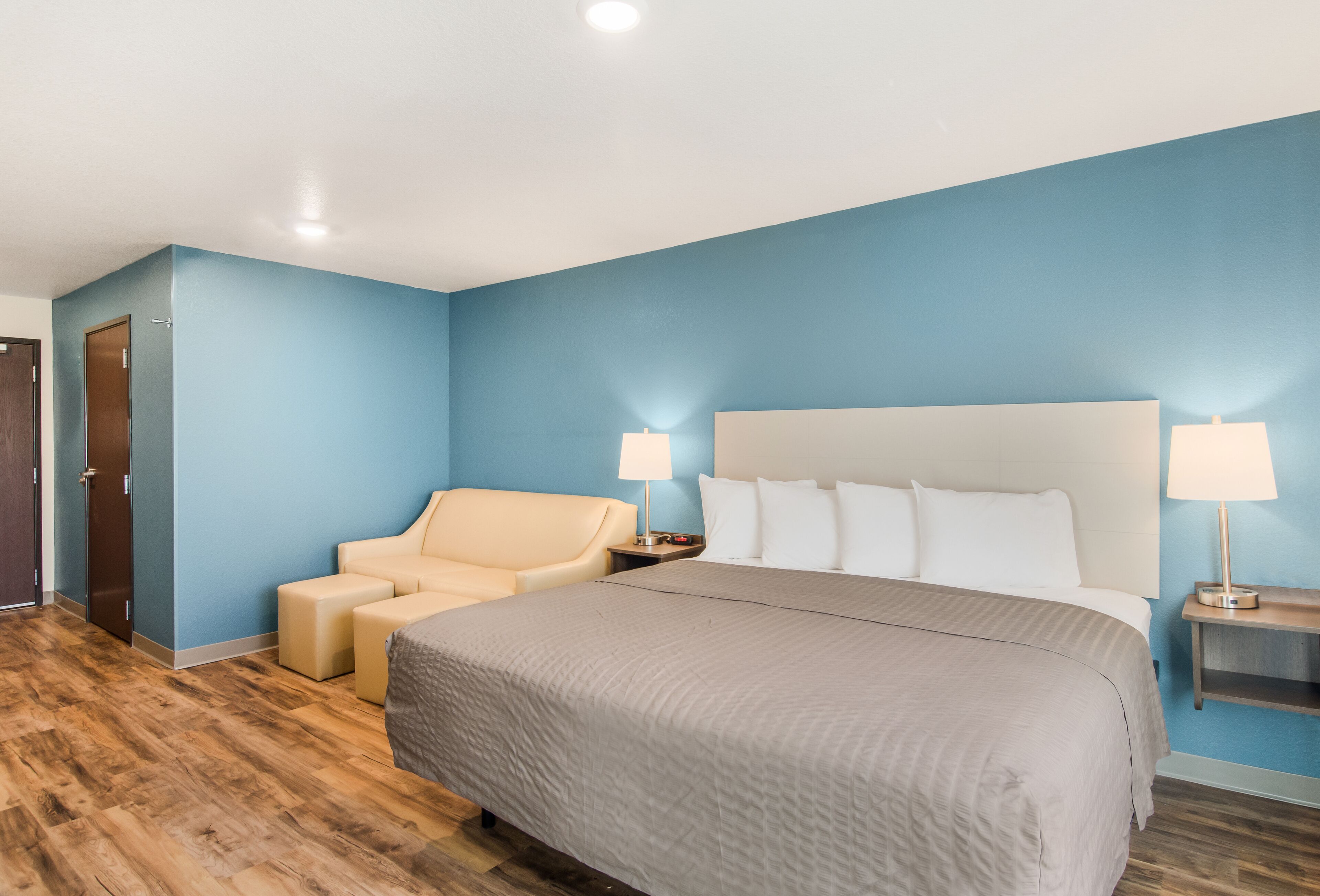 Una habitación de hotel con una cama grande, una silla, dos lámparas de noche y suelo de madera.
