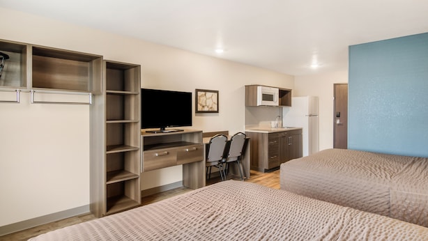 A compact hotel room with a bed, a desk with a chair, a television, a microwave, and a wardrobe. - WoodSpring Suites Thornton-North Denver (Thornton)