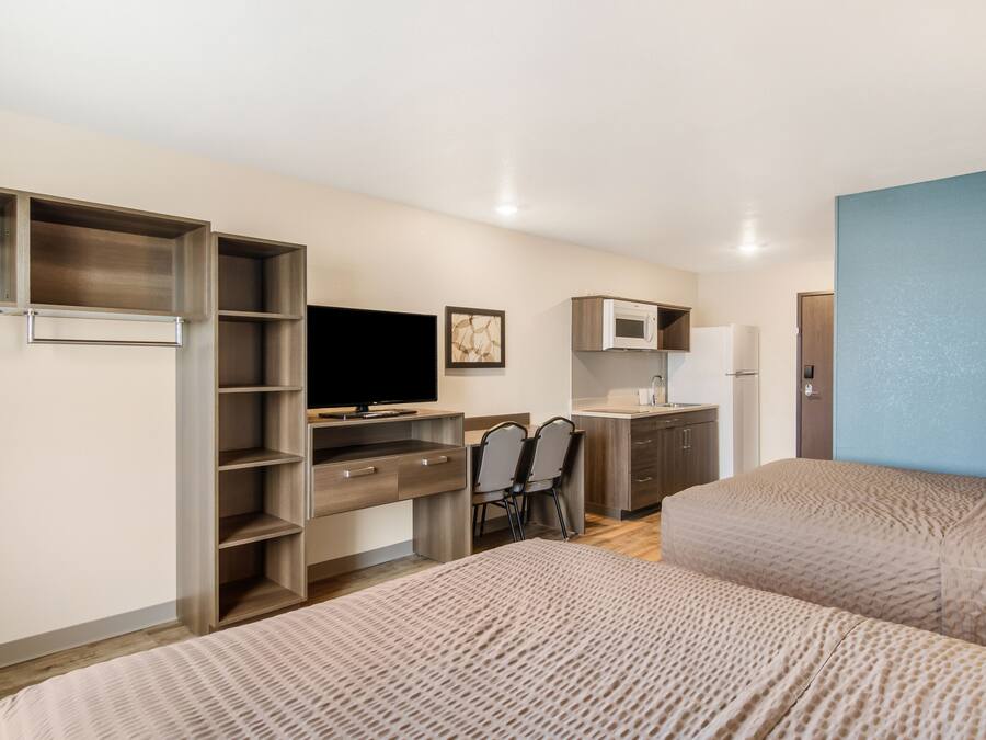 A compact hotel room with a bed, a desk with a chair, a television, a microwave, and a wardrobe.