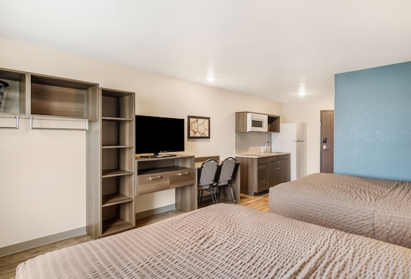 A compact hotel room with a bed, a desk with a chair, a television, a microwave, and a wardrobe. - WoodSpring Suites Thornton-North Denver (Thornton)