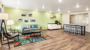 A modern living room with a sofa, coffee table, and a dining area with chairs. - WoodSpring Suites Thornton-North Denver (Thornton)
