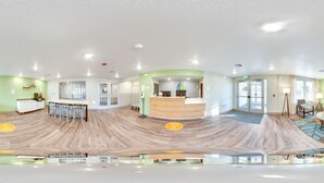 A panoramic view of a hotel lobby with a reception desk, seating area, and a large mirror. - WoodSpring Suites Thornton-North Denver (Thornton)