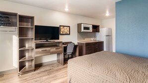 A compact hotel room with a bed, a desk with a chair, a TV, a microwave, and a refrigerator. - WoodSpring Suites Thornton-North Denver (Thornton)
