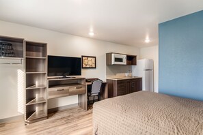 A compact hotel room with a bed, a desk with a chair, a TV, a microwave, and a refrigerator. - WoodSpring Suites Thornton-North Denver (Thornton)