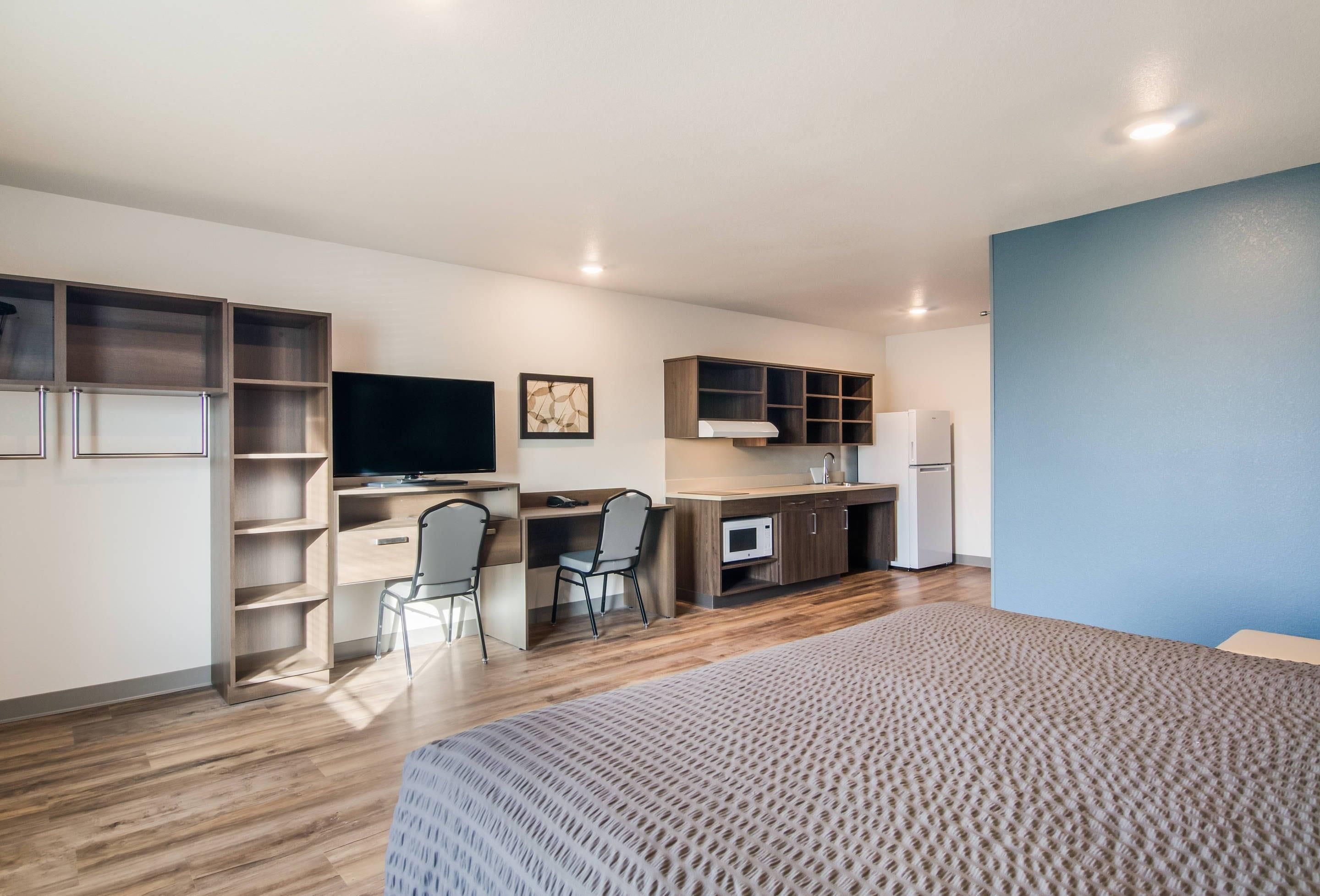 A compact room with a bed, a desk, two chairs, a television, a microwave, and a refrigerator.