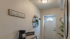 A hallway with a wooden coffee table, a sign saying "Stay Awake," a mirror, and a door with a window. - University Suite "C" (Marion)
