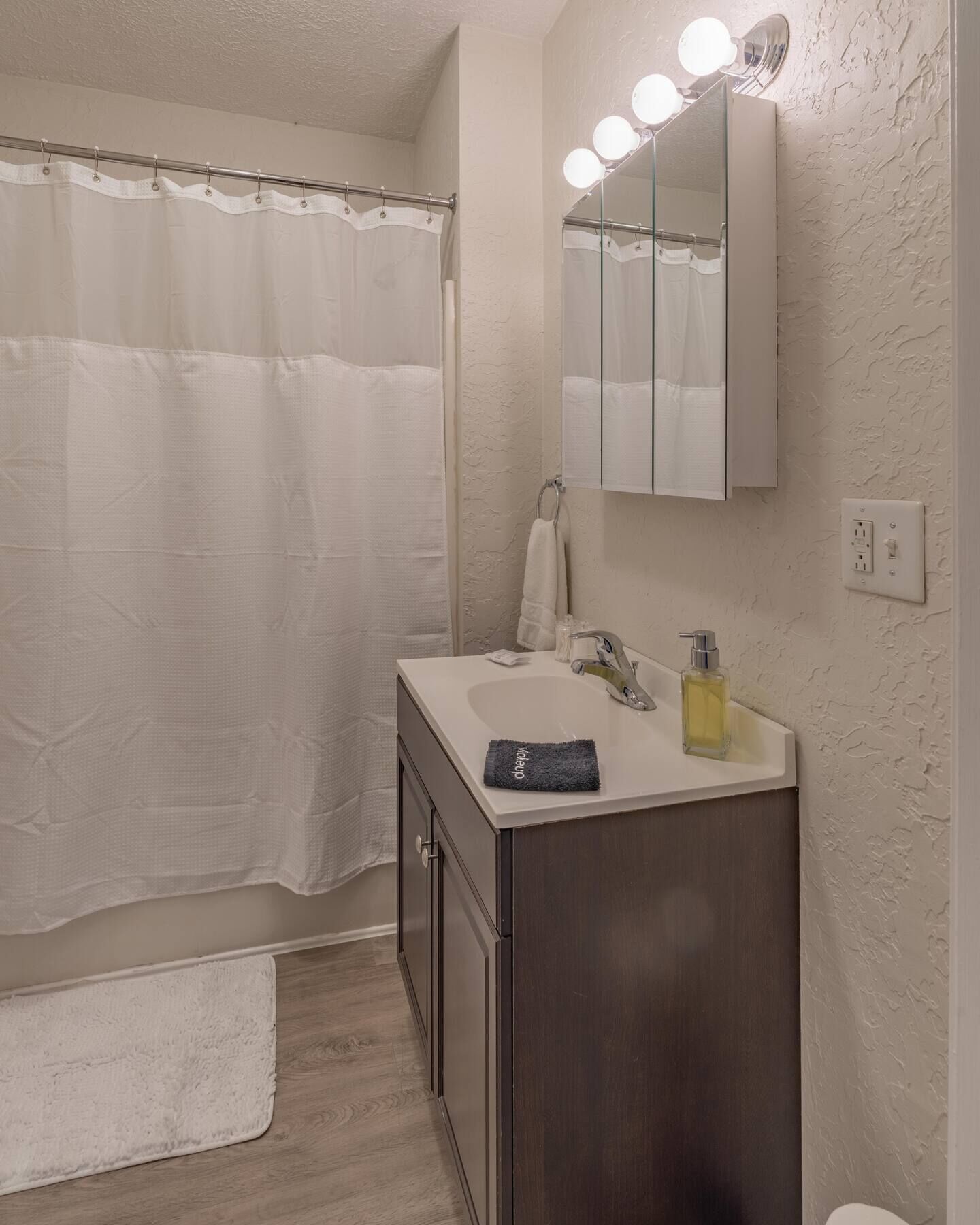 A bathroom with a shower curtain, a sink with a mirror, and a towel rack.