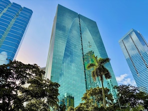 Un grand bâtiment moderne en verre, doté d’une façade réfléchissante, entouré d’arbres et d’autres immeubles.