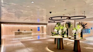 Un hall d’hôtel moderne, doté d’un comptoir d’accueil, de tables rondes ornées de compositions florales et d’un sol ciré.