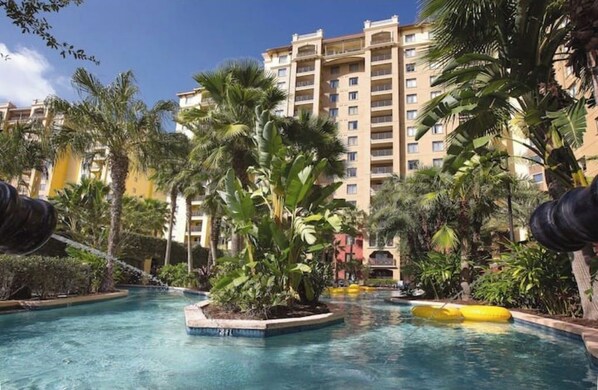 Relax by the pool surrounded by lush greenery and tropical plants, with a view of the surrounding buildings.