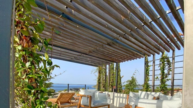 Une terrasse sur le toit, dotée de chaises en bois et d’une pergola, qui offre une vue sur une étendue d’eau.