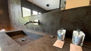 Une salle de bain moderne avec un grand lavabo, un miroir et deux distributeurs en verre posés sur le comptoir.