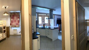 A narrow hallway with bunk beds on both sides, a kitchen area with cabinets and a sink, and a staircase with a wooden railing. - D305 - 73m2 - 4P - 8/10 pers (Prapoutel)