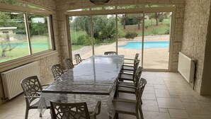 Une terrasse couverte avec une table et des chaises, des murs en pierre et une vue sur une piscine.