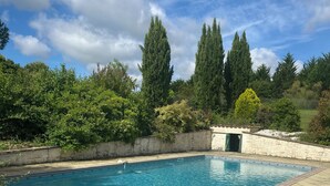 Une piscine dotée d’une terrasse en bois, entourée de verdure et de grands arbres.