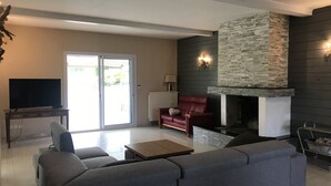 Un salon moderne avec une cheminée en pierre, un canapé rouge, un canapé d’angle gris et un téléviseur à écran plat posé sur une table en bois.