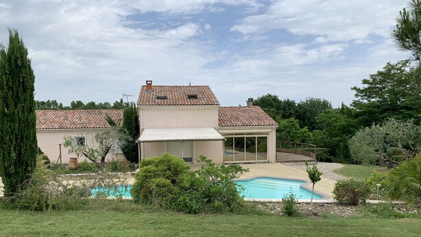 Une maison avec une piscine, entourée d’une pelouse bien entretenue et de divers arbres.