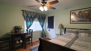 Ein Schlafzimmer mit einem Bett, einem Schreibtisch mit Stuhl, einem Deckenventilator und einer Tür.