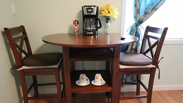 Ein runder Holztisch mit zwei Stühlen, einer Kaffeemaschine und zwei Tassen auf einem Regal.