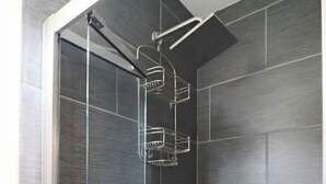 Eine moderne Dusche mit Glastür, dunklen Fliesen und einem Chrom-Duschkopf.