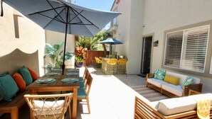 Eine Terrasse im Freien mit Holztisch, Stühlen, einem blauen Sonnenschirm und einer Couch.